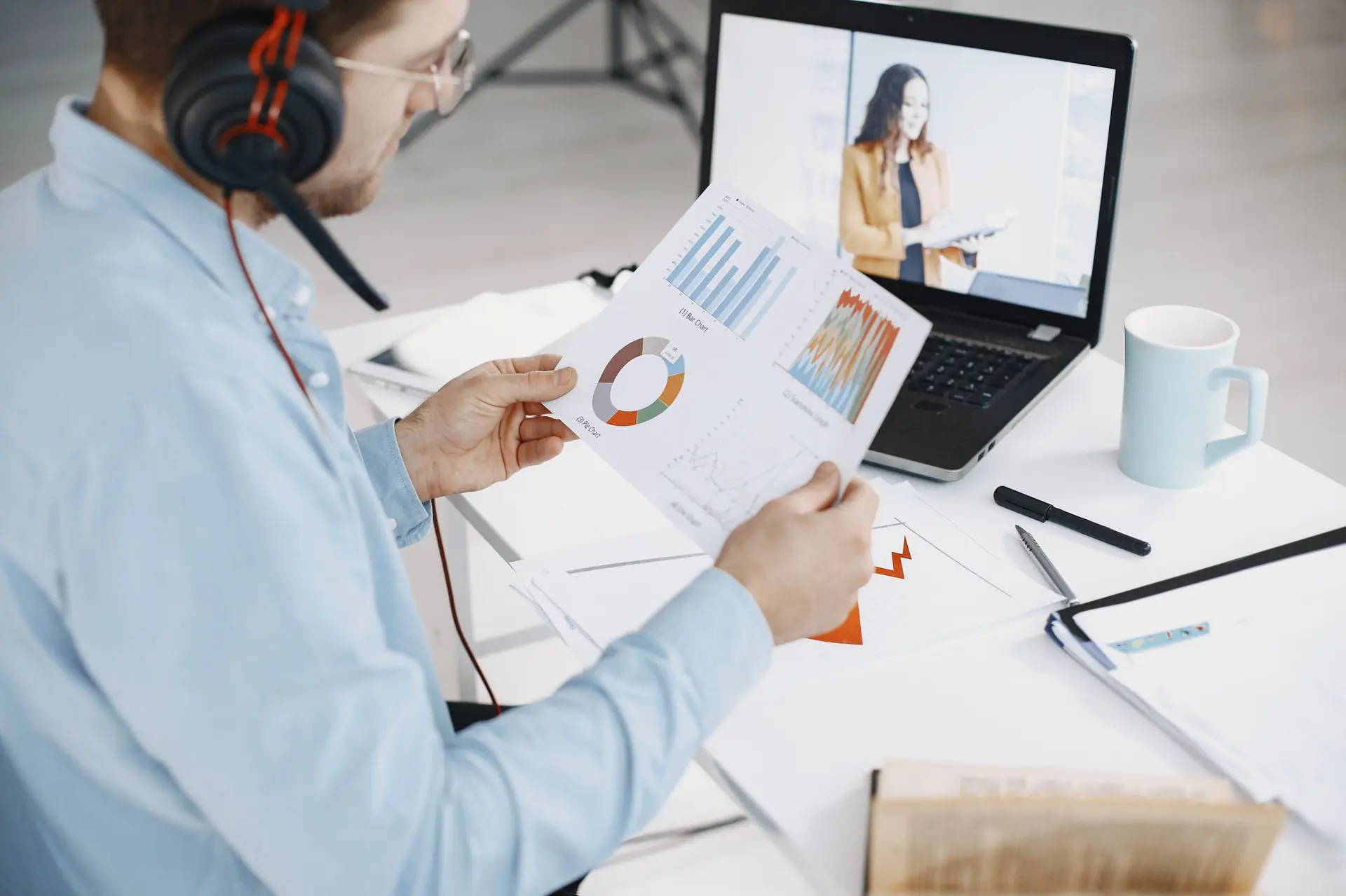 A person on a video call reviewing printed charts on a desk